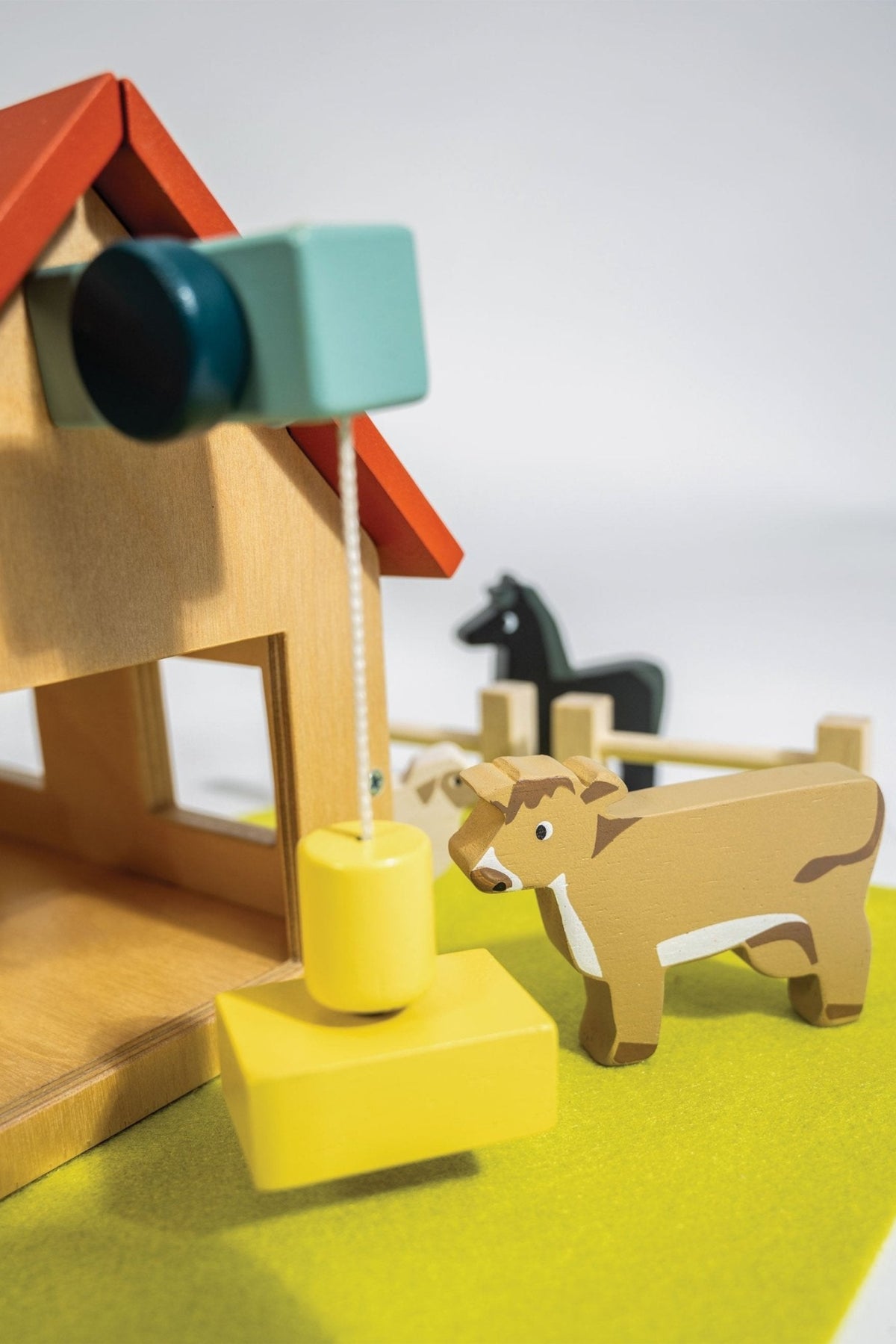 A colorful wooden playset features a barn with a red roof and a yellow pulley system. A painted cow stands nearby, set against a bright green base.