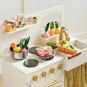 A wooden play kitchen setup features vibrant, organic food items, including pretend meats, vegetables, and condiments, encouraging imaginative play. The kitchen includes a sink, pots, and colorful accessories.