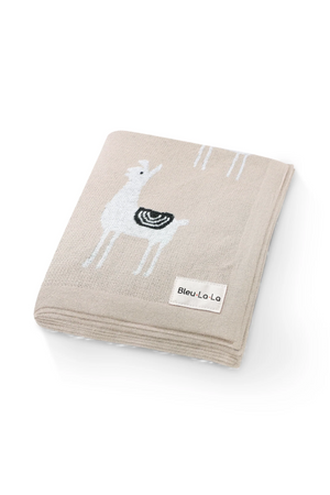 A beige knit blanket with white llama patterns and a Bleu La La label on the corner.