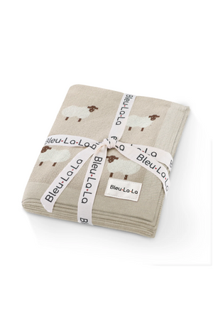 Folded beige blanket with sheep pattern, tied with a branded Bleu-La-La ribbon on a white background.