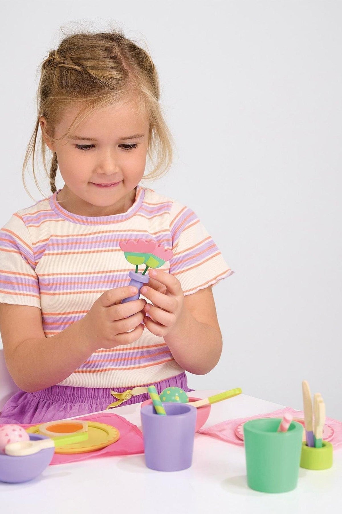 A child in a striped shirt plays with colorful wooden toys at a table set with pretend play items.