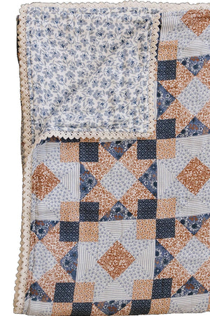 A twin muslin quilt featuring a patchwork design in blue, orange, and cream, with a delicate lace edge.
