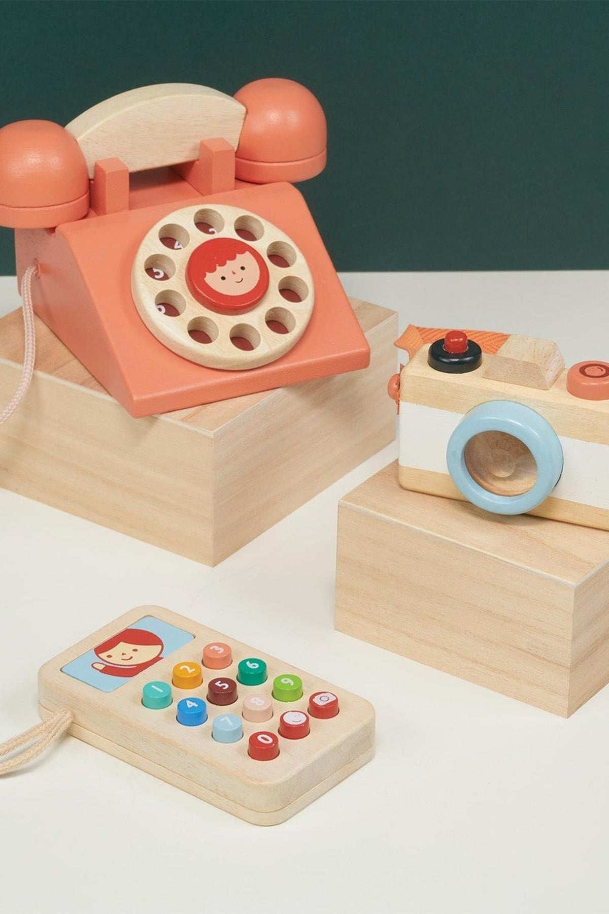 Wooden toy set featuring a retro telephone, camera, and mobile phone with colorful buttons, on display blocks.