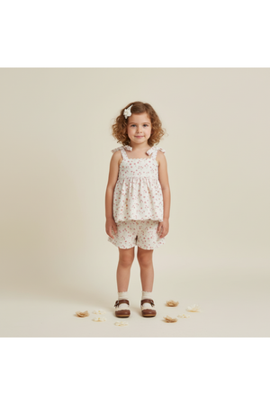 A young girl stands smiling in a light pink tie-up top and matching shorts set adorned with floral patterns.