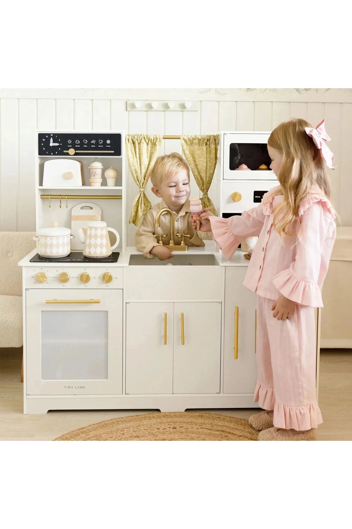 Two children play with the Tiny Land® Iconic Wooden Play Kitchen, featuring a cream color and gold accents. The kitchen includes realistic appliances and encourages imaginative cooking play.
