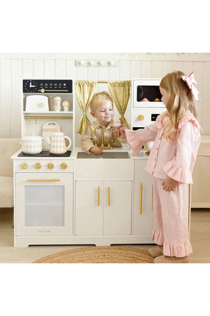 Two children play with the Tiny Land® Iconic Wooden Play Kitchen, featuring a cream color and gold accents. The kitchen includes realistic appliances and encourages imaginative cooking play.