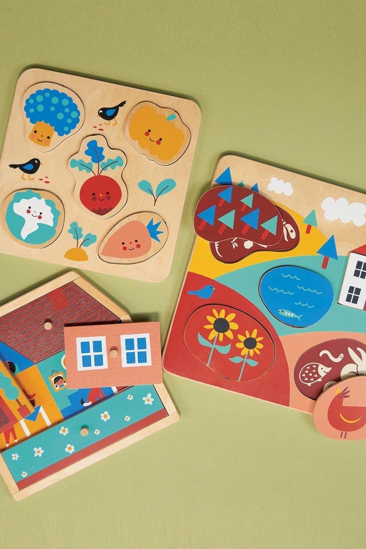 Three colorful wooden puzzles featuring vegetables, a house, and a countryside scene on a green background.