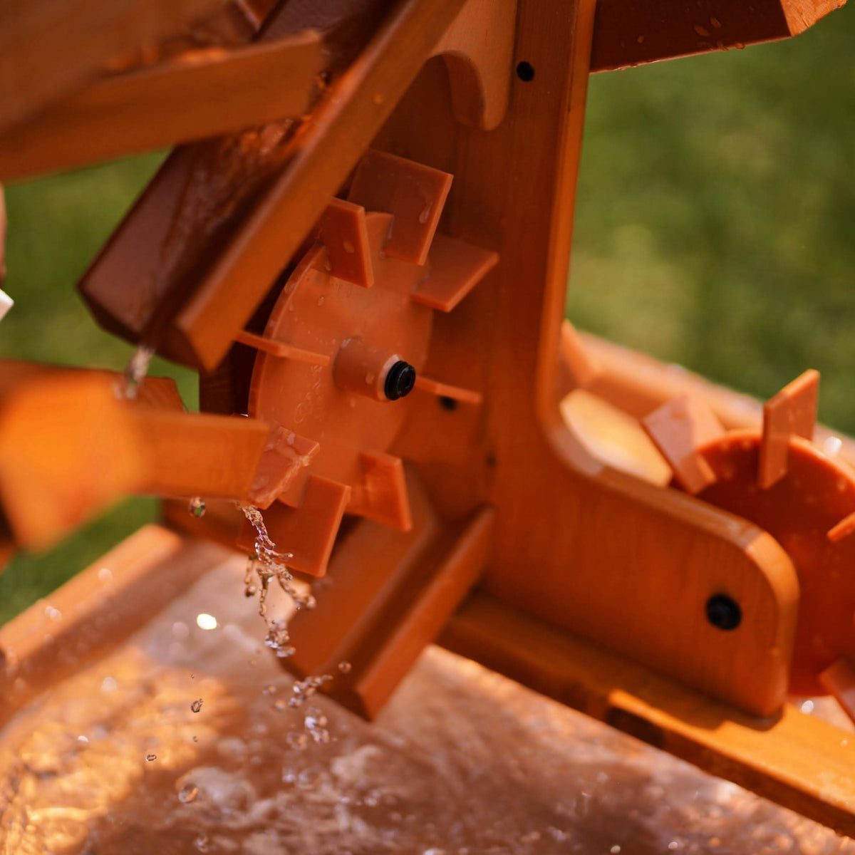 Close-up of a wooden water table featuring a water wheel, with clear water flowing over the wheel. The natural wood finish highlights its eco-friendly design, perfect for toddler sensory play.