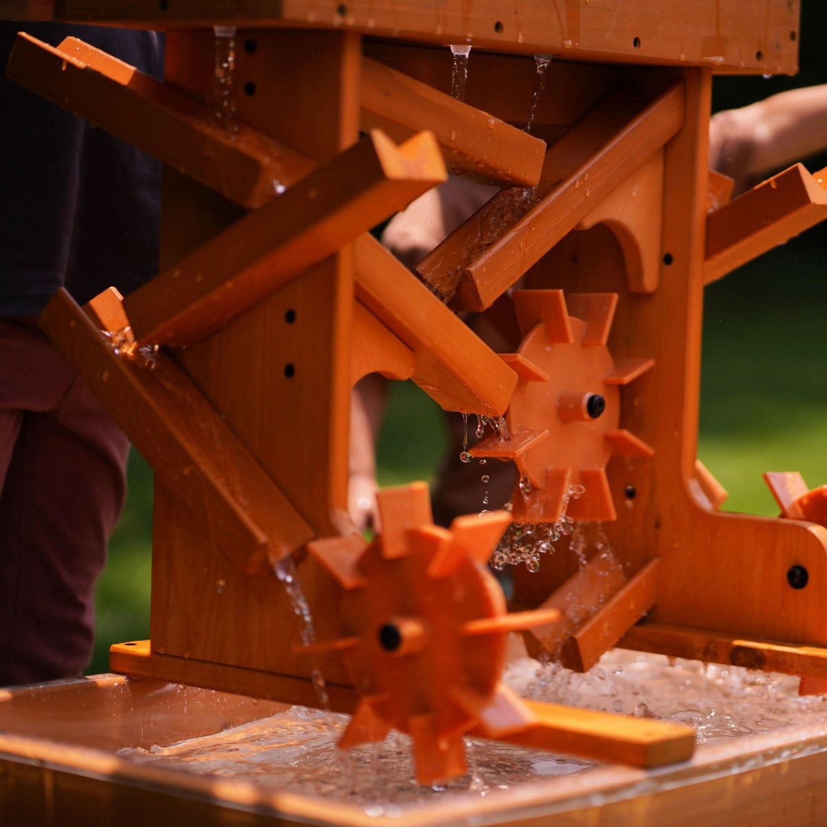 A vibrant outdoor wooden water table features spinning wheels and flowing water, designed for sensory play. Ideal for toddlers, it encourages exploration and learning through hands-on activities.