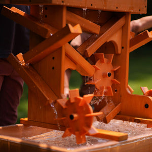 A vibrant outdoor wooden water table features spinning wheels and flowing water, designed for sensory play. Ideal for toddlers, it encourages exploration and learning through hands-on activities.