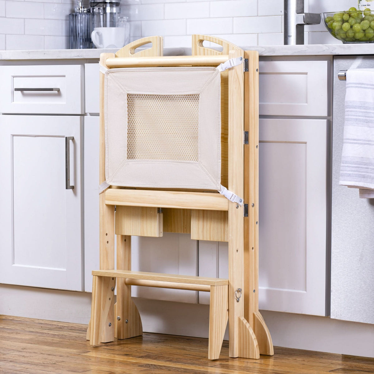 A wooden foldable kitchen tower with a mesh panel stands against a white cabinet, featuring a built-in step stool and storage compartments, ideal for engaging toddlers in cooking activities.