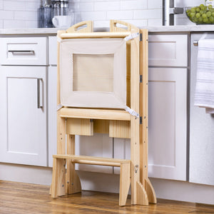 A wooden foldable kitchen tower with a mesh panel stands against a white cabinet, featuring a built-in step stool and storage compartments, ideal for engaging toddlers in cooking activities.