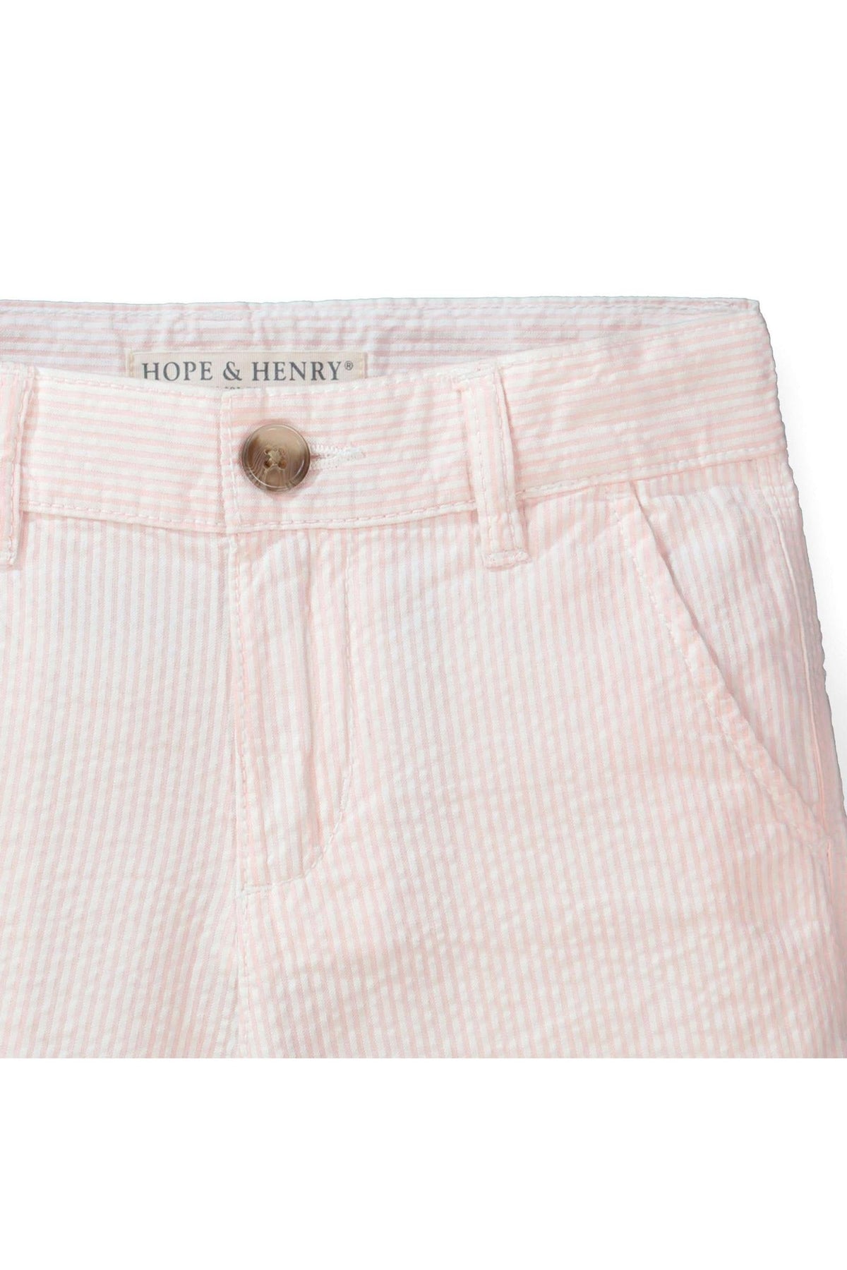 Close-up of light pink organic cotton seersucker shorts by Hope & Henry, featuring a faux horn button and subtle striped texture, designed for comfort and style in childrens casual wear.