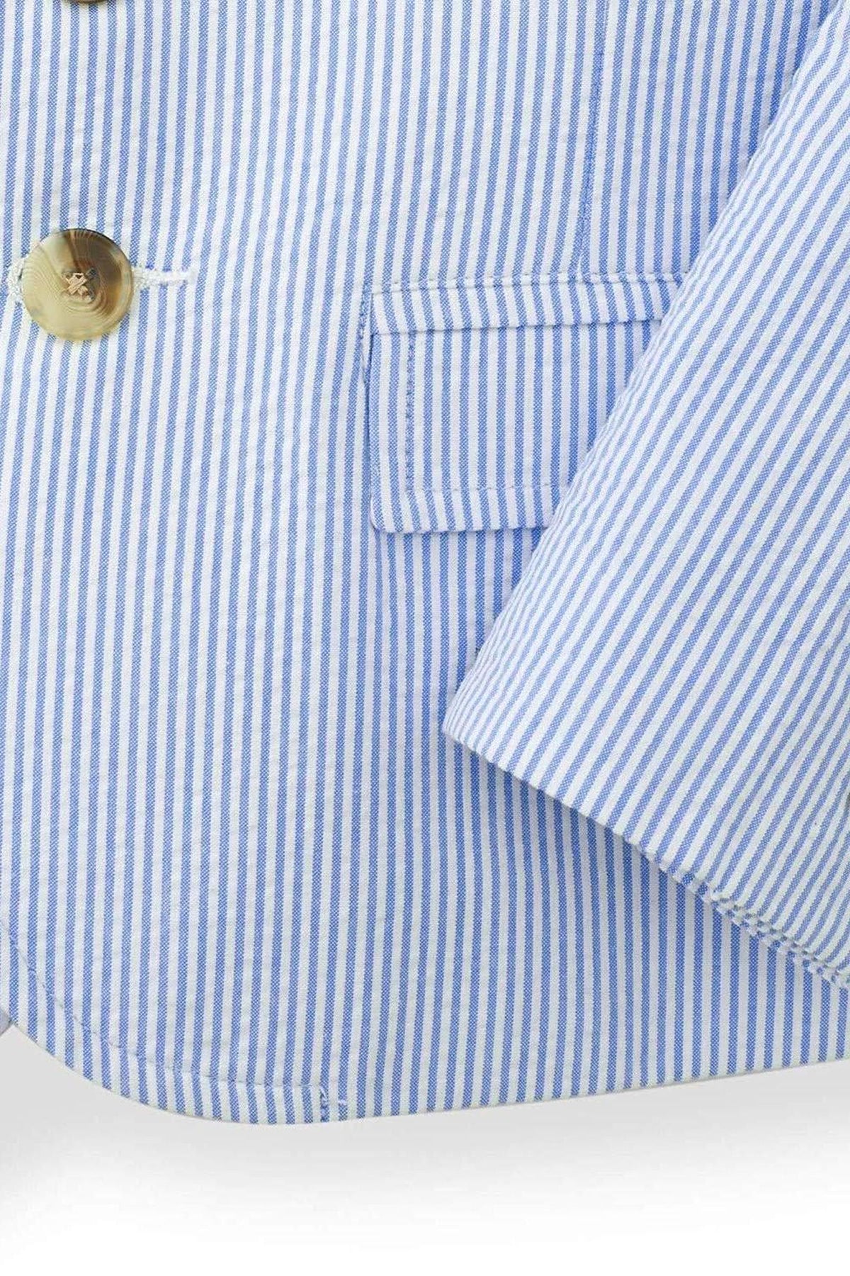 Close-up of a boys traditional seersucker suit jacket in blue and white stripes, featuring a notch collar, faux horn buttons, and a welt chest pocket, made from 100% organic cotton.