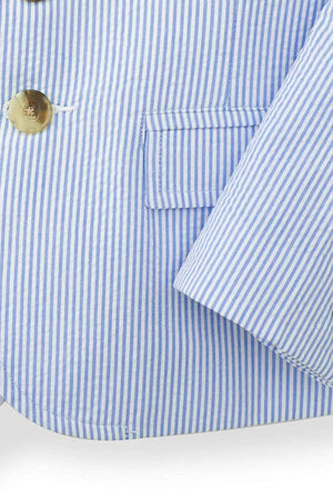 Close-up of a boys traditional seersucker suit jacket in blue and white stripes, featuring a notch collar, faux horn buttons, and a welt chest pocket, made from 100% organic cotton.