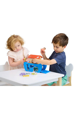 Two children play with a blue and red wooden ark toy, sorting animal-shaped pieces on a white table.