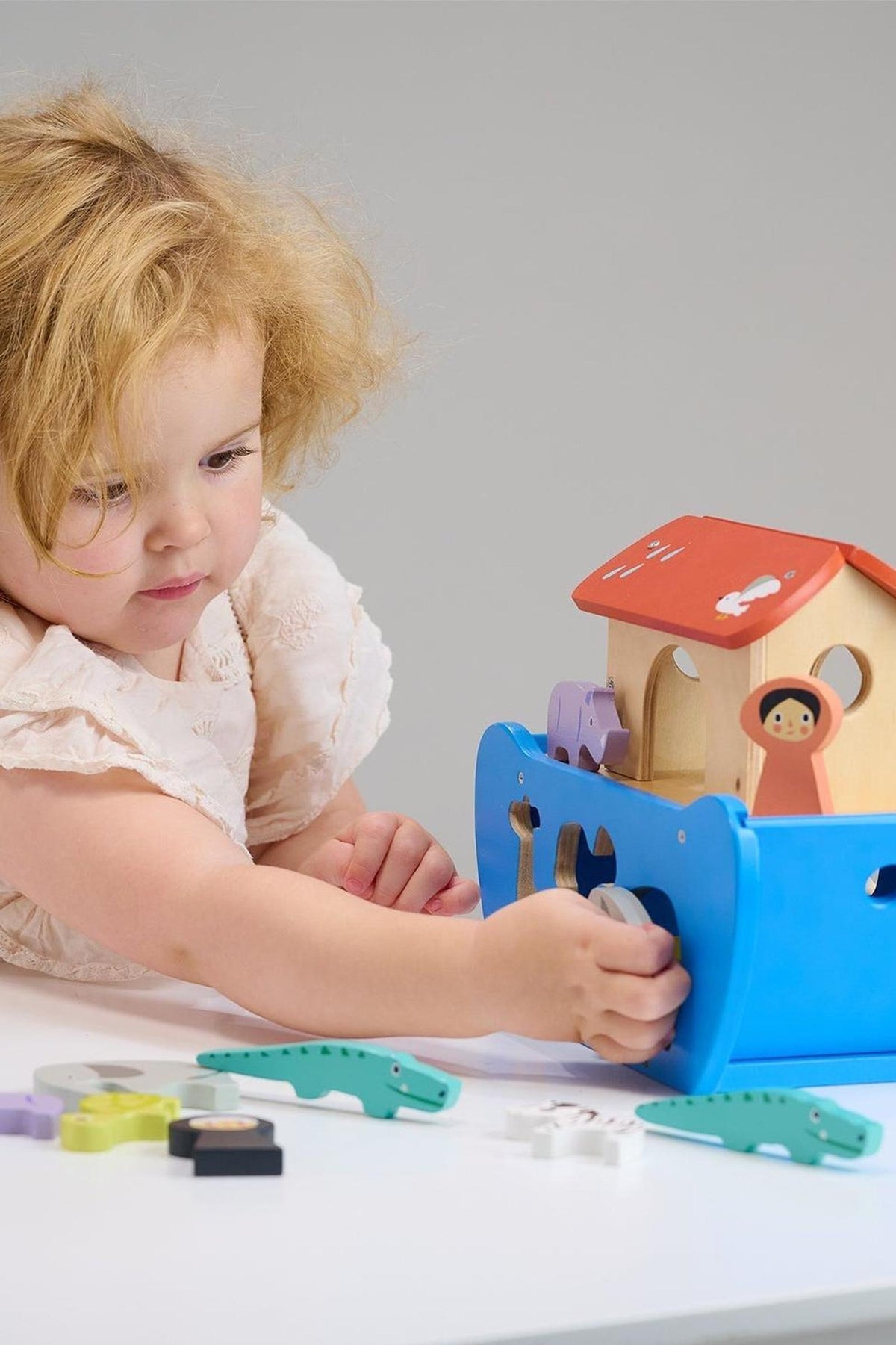 A child plays with a colorful wooden animal ark toy, featuring a blue boat and various animal shapes.