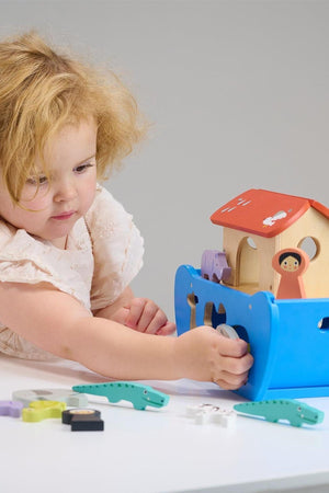 A child plays with a colorful wooden animal ark toy, featuring a blue boat and various animal shapes.