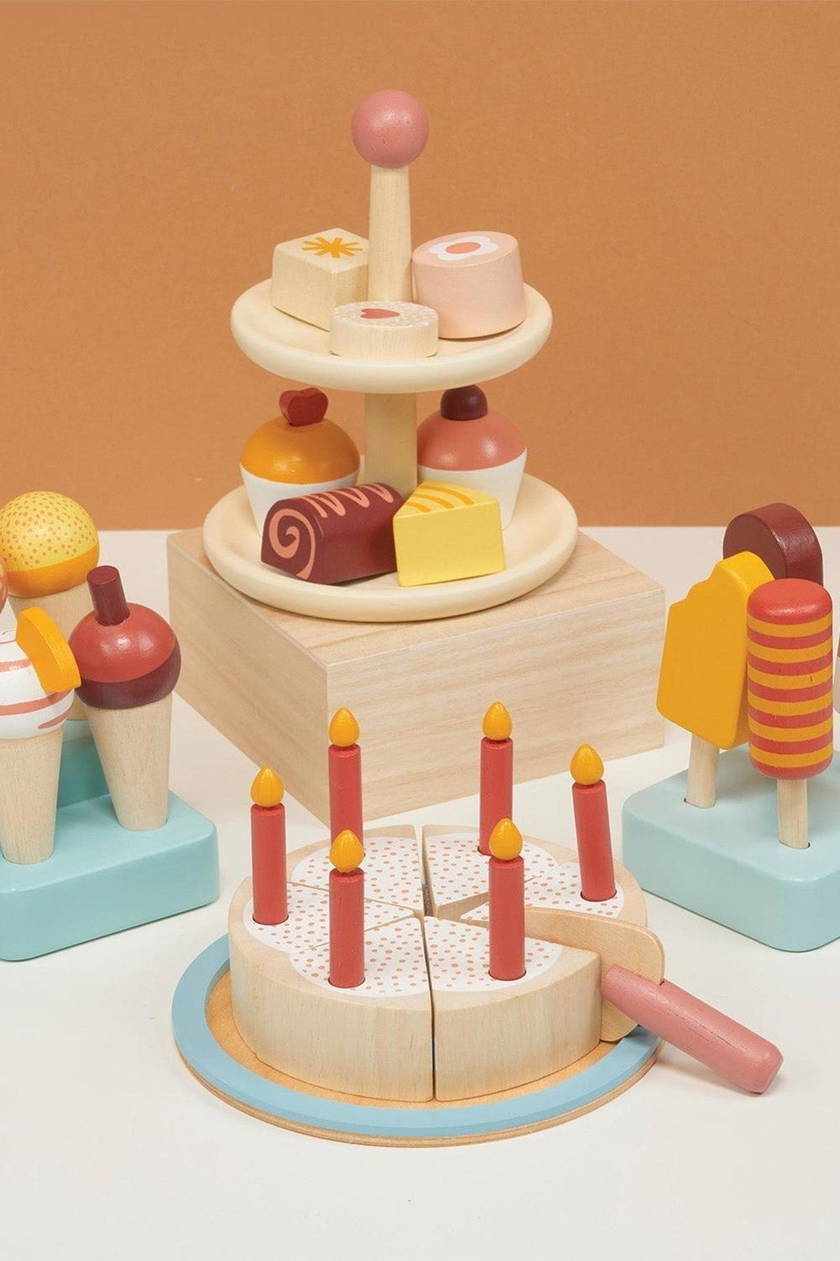 Wooden toy set featuring cake slices with candles, lollipops, and tiered pastries on a light wood base.