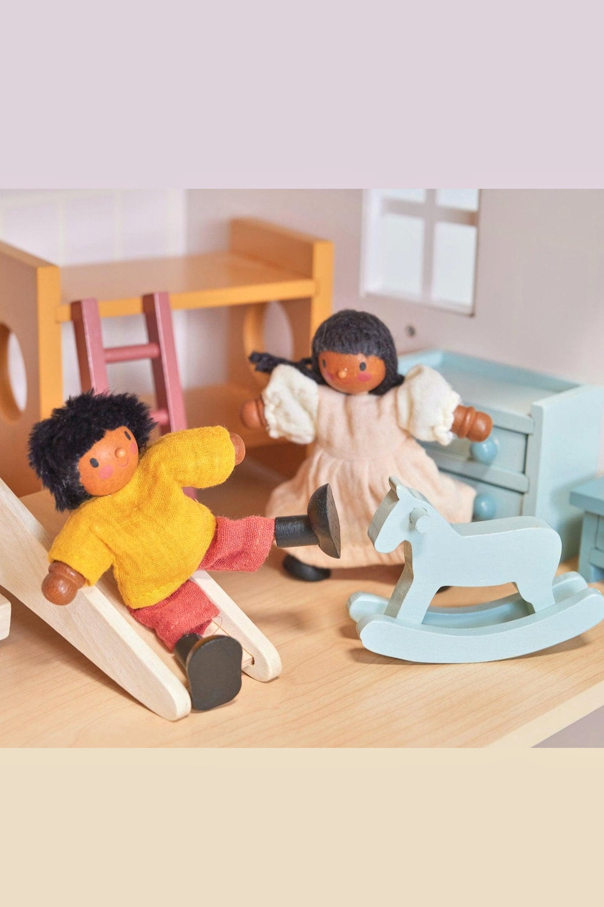 Two wooden dolls with bendy limbs, one sliding, the other near a blue rocking horse, in a dollhouse setting.