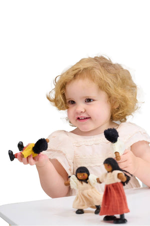 A child in a white dress is playing with colorful wooden dolls featuring bendable limbs and fabric clothing.