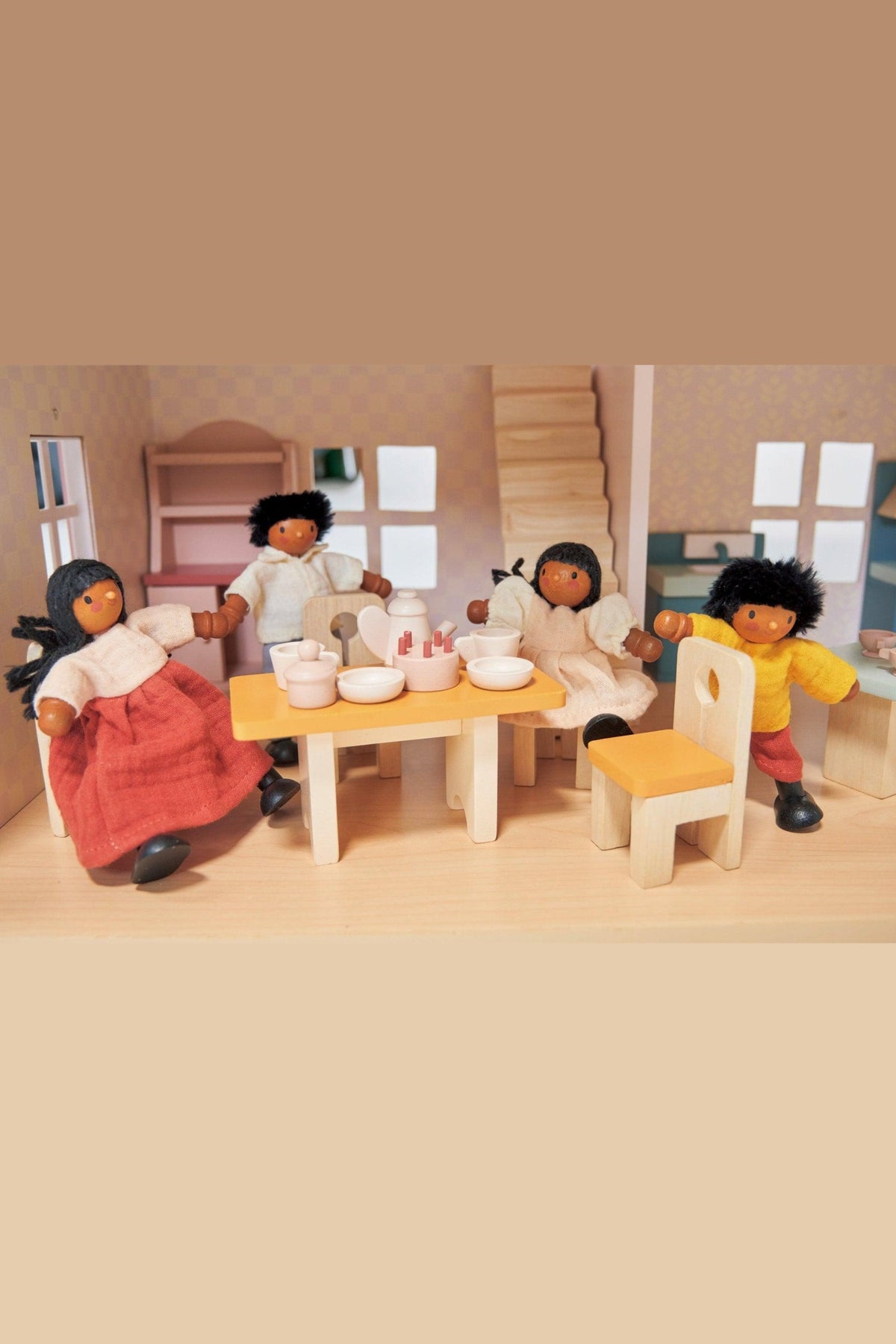 Four wooden dolls with colorful clothing sit around a wooden table in a dollhouse dining room.