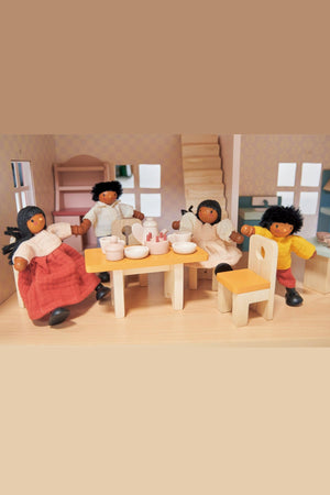 Four wooden dolls with colorful clothing sit around a wooden table in a dollhouse dining room.
