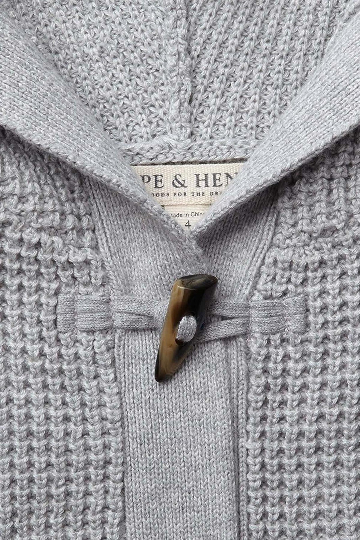 Close-up of a gray hooded sweater with a waffle stitch texture, featuring a faux horn toggle and visible brand label.