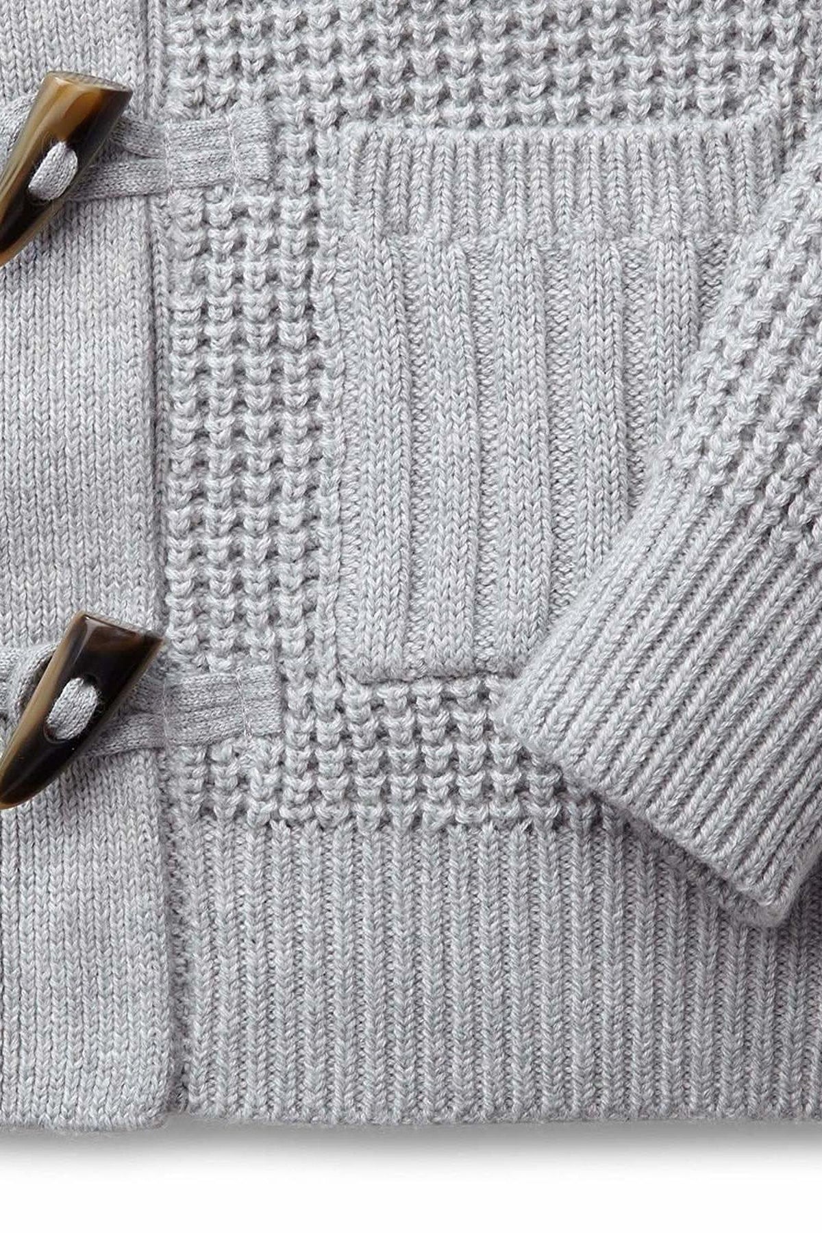 Close-up of a gray waffle knit baby sweater featuring faux horn toggles and ribbed front pockets, made from organic cotton.