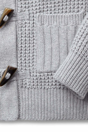 Close-up of a gray waffle knit baby sweater featuring faux horn toggles and ribbed front pockets, made from organic cotton.