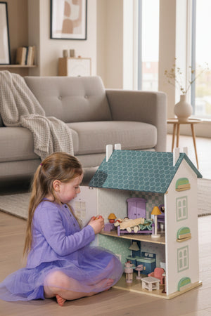 Young girl playing with a dollhouse in a room with pink walls.
