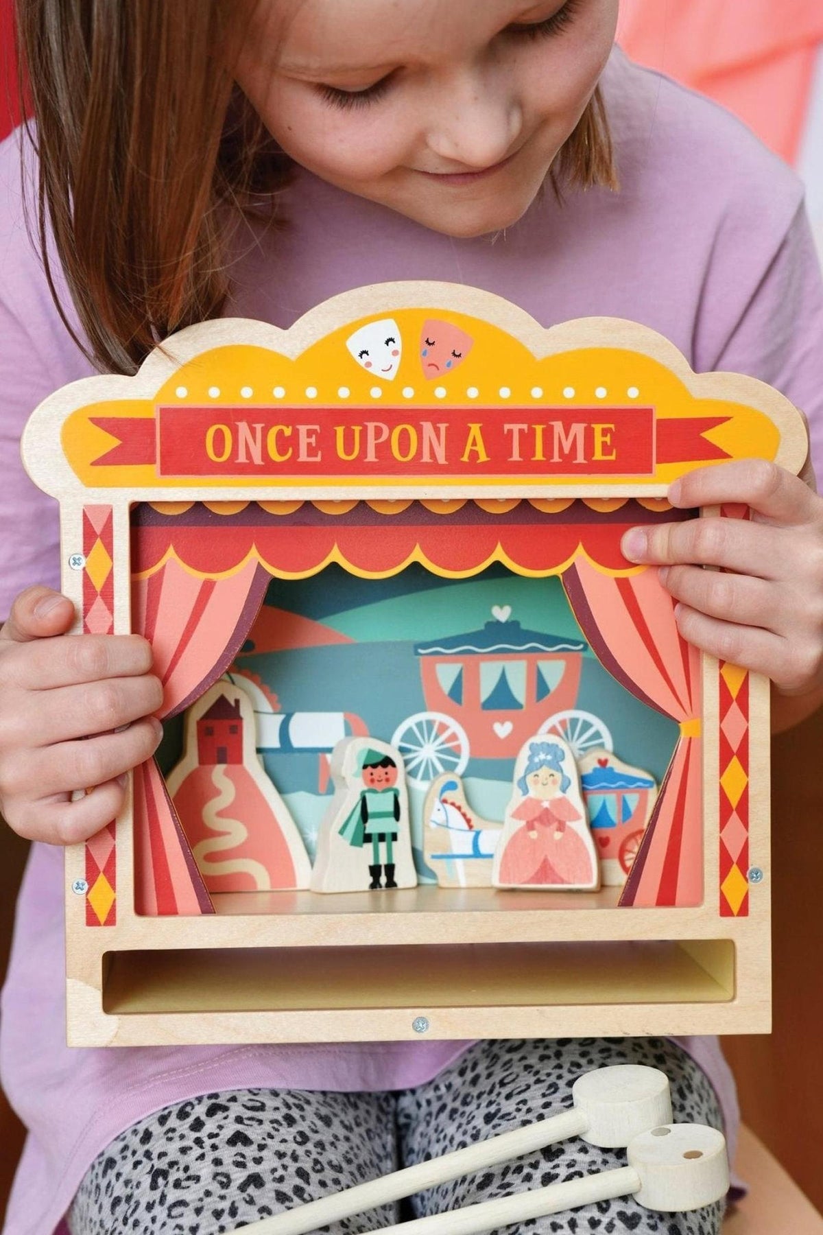 A child holds a colorful wooden tabletop theater with Once Upon a Time text, featuring illustrated characters and scenery.